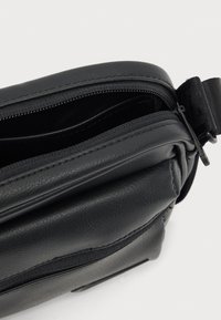 Μαύρο δερμάτινο τσαντάκι ώμου με φερμουάρ, με υφή στην επιφάνεια και ρυθμιζόμενο ιμάντα. Κομψός σχεδιασμός με πλαϊνή τσέπη.