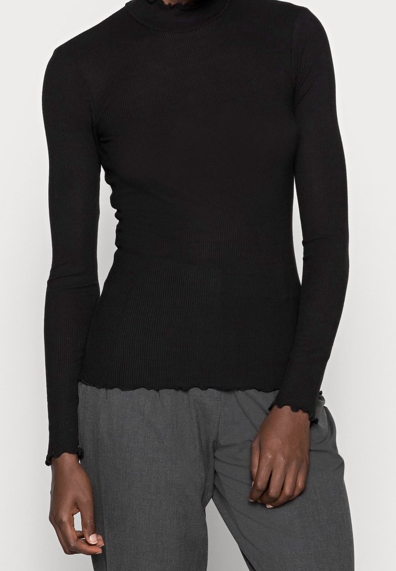 Schwarzes, geripptes Langarm-Turtleneck-Oberteil mit gewelltem Saum und Ärmelabschlüssen, kombiniert mit grauen, strukturierten Hosen. Weiches Material und figurbetontes Design.