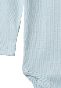 Gros plan sur le tissu côtelé bleu clair d'un body bébé à manches longues, montrant les bords des manches et des ouvertures pour les jambes.