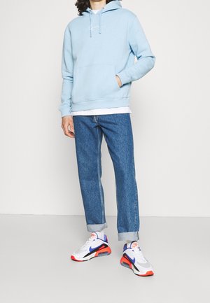 Sudadera azul clara con bolsillo frontal, llevada sobre una camiseta blanca. Combinada con jeans azules remangados y zapatillas multicolores.