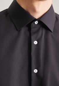 Camisa negra con cuello que presenta una textura suave, cinco botones blancos con hilo negro y un diseño estructurado.