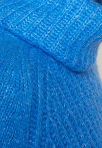 Gros plan sur un tissu tricoté bleu doux montrant une texture côtelée et duveteuse détaillée.