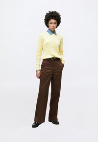 Pull en maille jaune avec un col bleu, assorti à un pantalon marron à jambes larges et des chaussures noires. La tenue présente un design texturé.