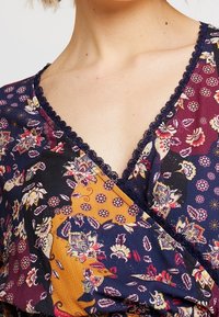 Bloemenprint wikkeltop met een V-halslijn, in marineblauw, oranje en bordeauxkleurige tinten. Delicate kantafwerking langs de halslijn. Gladde stofstructuur.