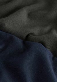 Twee stukken stof: één donkergroen en één marineblauw, beide met een gladde, zachte textuur en een subtiele breipatron.