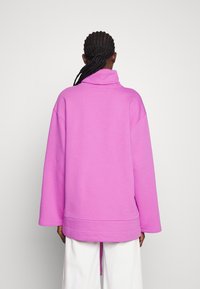 Sudadera rosa de gran tamaño con cuello alto, hombros caídos y mangas largas. Cuenta con un dobladillo con una abertura lateral. Tejido suave y texturizado.