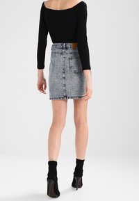 Falda corta de denim en azul claro con dobladillo deshilachado, que cuenta con bolsillos traseros y una cintura alta. Combinada con botas de calcetín negras con tacón.