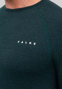 Ciemnozielona sportowa koszulka z teksturowanej tkaniny, z okrągłym dekoltem i logo "FALKE" w białym kolorze na wysokości klatki piersiowej.