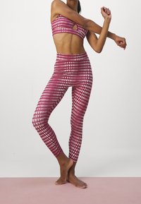 Růžový a bílý vzorovaný sportovní set, který se skládá z bandeau topu a legín s vysokým pasem, zdobených geometrickým designem a hladkou texturou.