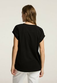 Czarna koszulka z krótkim rękawem, prostej formie i okrągłym dekoltem. Gładka tekstura, prosty wzór, bez widocznych wzorów czy akcentów.