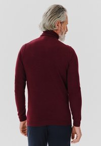 Burgundowa dzianinowa sweterka z golfem, z długimi rękawami, ściągaczami przy mankietach i u dołu, prezentująca gładką fakturę i dopasowany krój.