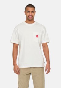 Weißes Baumwoll-T-Shirt mit Rundhalsausschnitt, kurzen Ärmeln und Brusttasche, die roten gestickten Text und Grafik über der Tasche zeigt.