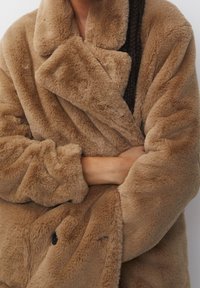 Manteau en fausse fourrure marron avec un col châle, une coupe ample et une surface texturée. Comprend deux gros boutons et un tissu épais et duveteux.