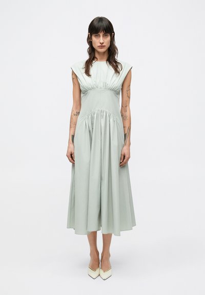 Light green knee-length dress with cap sleeves, gathered waist, and smooth fabric texture, paired with pointed white heels.