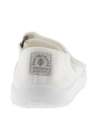 Zapato slip-on de lona blanca con superficie texturizada, tab en el talón con bucle y parche rectangular con el logo en la parte trasera. Suela de goma.