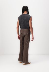 Brown wide-leg pants with white stitching and multiple pockets, paired with a gray sleeveless top. Displayed from the back.