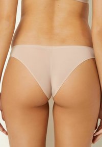 Slip bikini beige realizzati in tessuto liscio e elastico con copertura minimale, dotati di un design senza cuciture e aperture per le gambe a taglio alto.