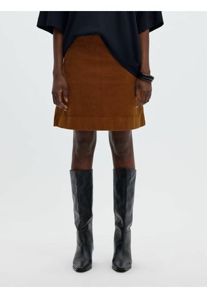 Personne portant une jupe en daim marron, des bottes en cuir noires montantes jusqu'aux genoux et un haut noir avec des bracelets à un poignet.