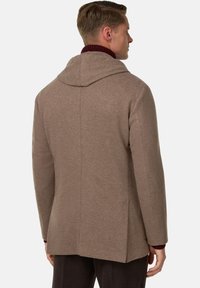 Brązowy wełniany płaszcz z kapturem, charakteryzujący się usztywnioną konstrukcją i gładką teksturą, widocznymi szwami oraz bordowym wewnętrznym kołnierzem.