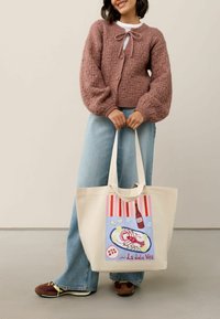 Bežová textilná taška s farebnou ilustráciou morských plodov, červenými pruhmi a textom "La dolce Vita." Taška má pevné uši.