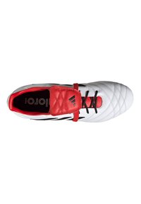 Scarpa da calcio bianca con una cinghia di gomma rossa, lacci neri e una tomaia testurizzata. Presenta una linguetta imbottita e un logo sulla cinghia.