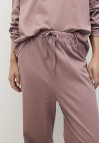 Joggers mauve clair en tissu doux, dotés d'une taille élastique avec cordon de serrage et poches latérales, texture lisse, coupe décontractée.