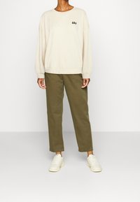 Sweat-shirt crème avec logo GAP, coupe décontractée, col et poignets côtelés, assorti à un pantalon fuselé vert olive et des baskets blanches.