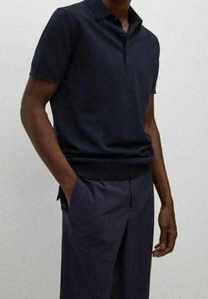Granatowa koszulka polo z krótkim rękawem i kołnierzykiem, z delikatną fakturą i slim fit. Połączona z ciemnymi spodniami, ręce w kieszeniach.