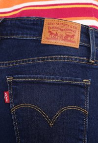 Mörkblå denimjeans med en läderlapp märkt "Levi Strauss & Co." och en röd Levi's-tagg på vänster ficka, med gul sömnad.