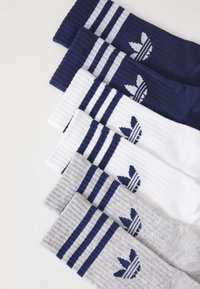 Trois paires de chaussettes à côtes de type crew en bleu marine, blanc et gris avec des rayures bleues et un logo en trèfle sur un fond blanc.