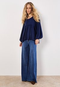 Navyblaues, strukturiertesLangarmoberteil mit gerafftem Bund, kombiniert mit weit geschnittenen blauen Jeans. Zarte Rüschendetails am Bund.
