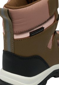 Bota marrón impermeable con parte superior texturizada en marrón y rosa, detalles en gris y suela de goma negra con borde blanco.