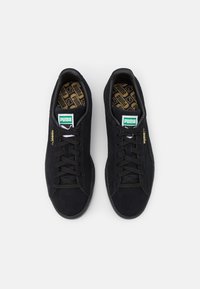 Schwarze Wildledersneaker mit einem Niedrigdesign, ausgestattet mit einer gemusterten Innensohle und tonalen Schnürsenkeln. Grünes Logotag auf der Zunge, minimalistische Markenkennzeichnung.