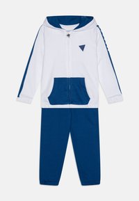 Balta zip-up džinsinė striukė su mėlynomis detalėmis, įskaitant priekines kišenes ir kapšelį. Prie striukės derančios mėlynos sportinės kelnės su elastinėmis rankovėmis. Pagaminta iš medvilnės.