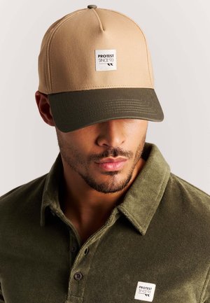 Man draagt een khaki en olijfgroene pet met het logo "PROTEST SINCE '93" en een bijpassend olijfgroen overhemd met kraag en dezelfde logopatch.