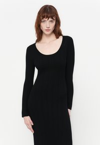 Black, long-sleeve dress with a scoop neckline, made of ribbed texture fabric, fitting closely to the body, reaching mid-calf length.