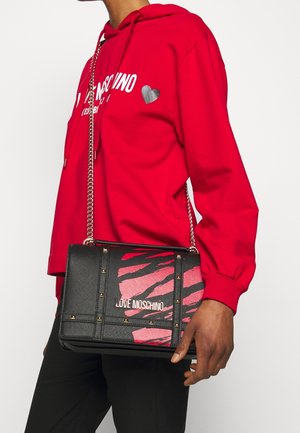Person trägt roten Love Moschino Hoodie und hält eine schwarze Love Moschino Handtasche mit pinkem Zebra-Muster und goldener Kettenriemen.