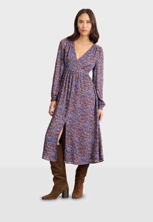 Robe maxi à motifs marron avec un décolleté en V profond, des manches longues et une fente haute jusqu'à la cuisse, assortie à des bottes marron jusqu'aux genoux.