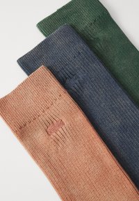 Tre paia di calzini a coste in rosa, blu navy e verde scuro. Ognuno presenta un piccolo dettaglio del logo vicino al bordo. Materiale morbido ed elastico.