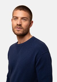 Dunkelblauer Pullover aus weichem Stoff, mit rundem Ausschnitt und Raglanärmel-Design; verfügt über feine Textur- und Stickdetails.