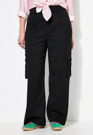 Zwarte cargo pants met wijde pijpen, voorzien van zijzakken en een soepele textuur. Gecombineerd met groene en roze sneakers.