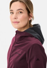 Bordeauxfarbener Kapuzenjacke mit einer dunkelgrauen Kapuze und schwarzen Akzenten. Verfügt über einen Reißverschluss und ein Logo auf der Brust und dem Ärmel. Glatte Textur.