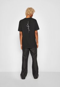 Black cotton t-shirt with a silver abstract design on the back, paired with loose-fitting dark denim pants and gray sneakers.