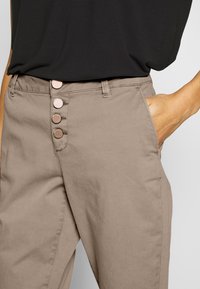 Beżowe bawełniane spodnie o dopasowanym kroju, z sześcioma guzikami z przodu, bocznymi kieszeniami i gładką fakturą.