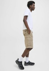 Beige cargo shorts with multiple pockets, paired with a plain white t-shirt and black athletic shoes, featuring white crew socks.