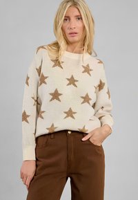 Maglione lavorato a maglia color crema chiaro con motivi a stella marroni, scollatura ampia e polsini a costine, abbinato a pantaloni marroni e hardware minimal in oro.