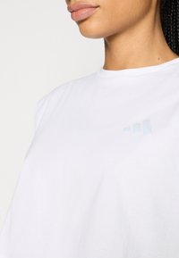 Άσπρη βαμβακερή μπλούζα με στρογγυλή λαιμόκοψη, με ανοιχτό μπλε λογότυπο Adidas στο αριστερό στήθος και άνετη εφαρμογή.