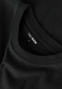 Mustast puuvillast T-särk, millel on ümmargune kaelus ja pehme tekstuur; sildi sees on kiri "TWO SOON," suurus L.