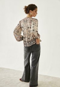 Blusa floral clara con mangas largas y flojas, cintura peplum, tejido suave en color beige; combinada con unos jeans de campana de talle alto en gris oscuro.