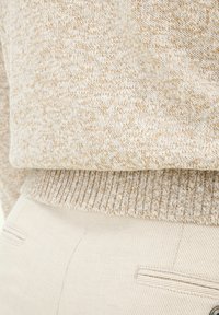 Beige knitted sweater with flecked texture and ribbed hem, paired with light beige pants featuring vertical stripes and side pockets.